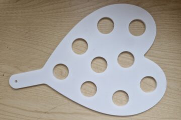 Image depicts previous work by CreativeCNC. Product shown is an acrylic shot glass holder in the shape of a heart. This product was custom-made for a local pub, and has space for nine shot glasses. The edges are smooth and precise.